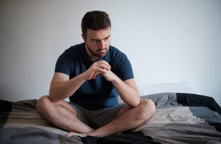 Depresijas nomākts vīrietis sēž uz gultas un jūtas slikti